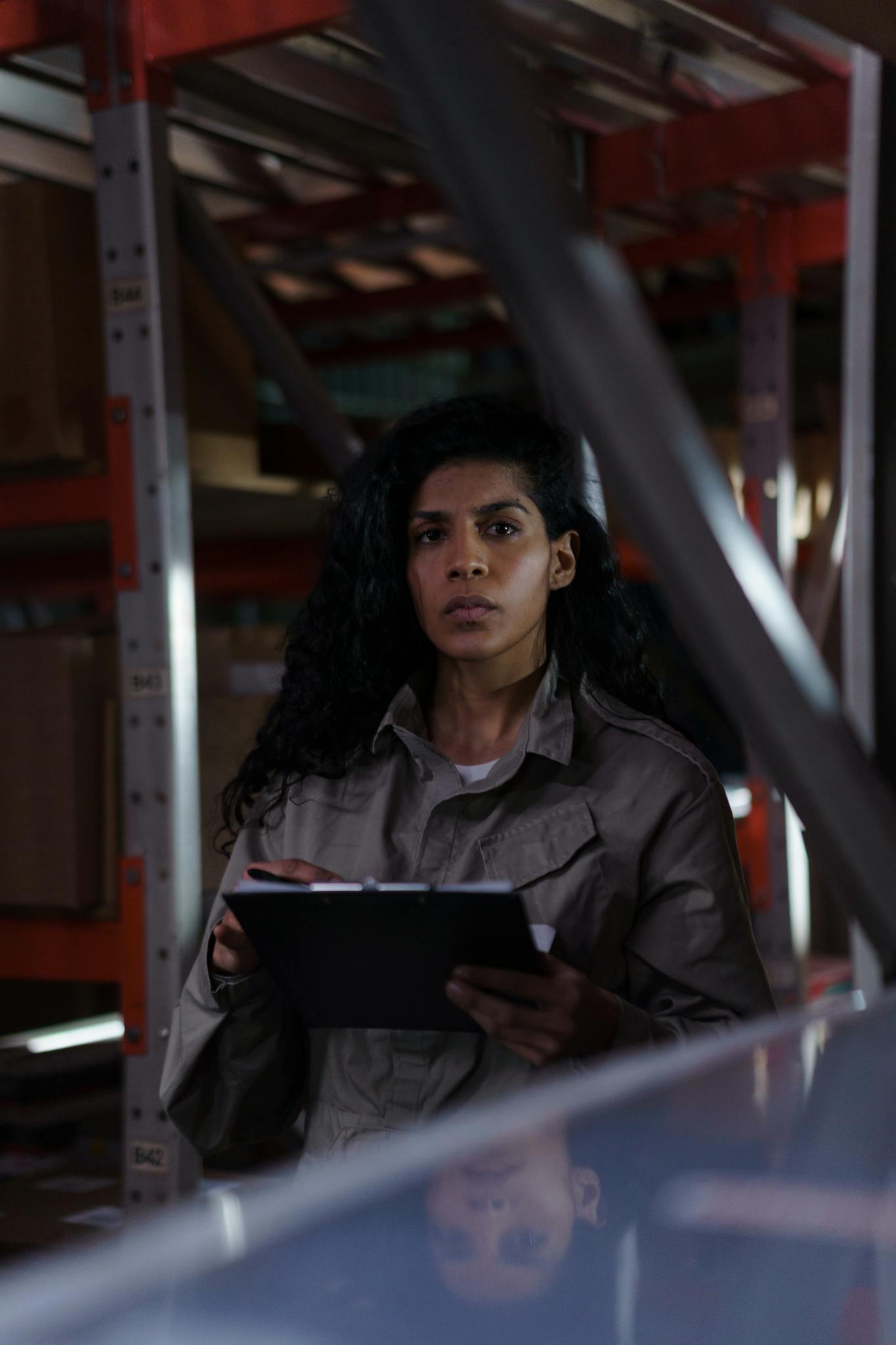 A focused woman holding a clipboard conducting an inventory check in a warehouse aisle.